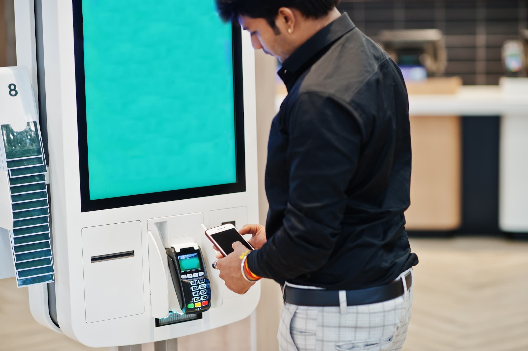 A man uses self-service kiosks to place an order at a quick service restaurant. 